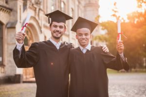 Bei laureati in abiti accademici sono in possesso di diplomi, guardano la macchina fotografica e sorridono mentre sono in piedi all'aperto
