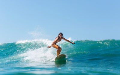 Bella giovane ragazza bruna in bikini costume da bagno cavalcare l'onda. Donna surfista sportiva che naviga a Mauritius nell'Oceano Indiano sullo sfondo di cielo blu, nuvole e onde trasparenti. Attivo all'aperto.